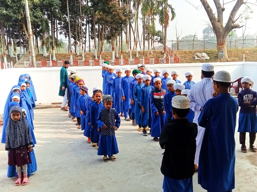Madrasa students in blue uniforms gathered outdoors at a school courtyard in Bangladesh